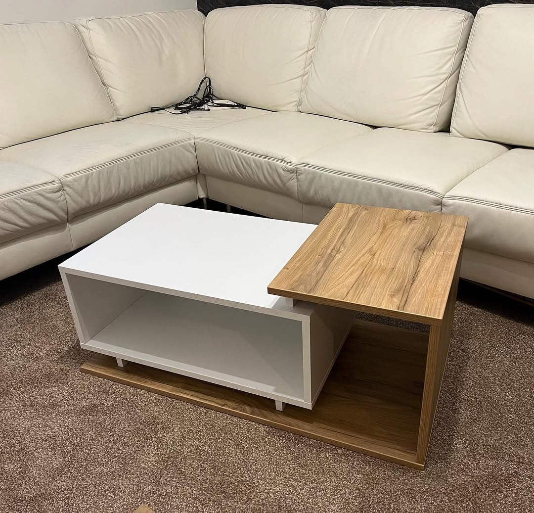 Modern coffee table with white and wood finishes placed on carpet in front of beige sectional sofa.