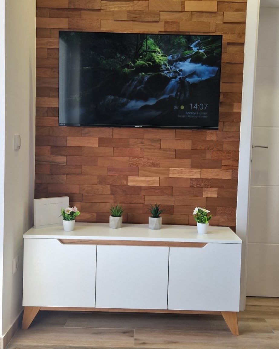 Wall-mounted flat-screen TV above a white cabinet with wooden legs and four small potted plants on top, set against a wood-paneled wall.