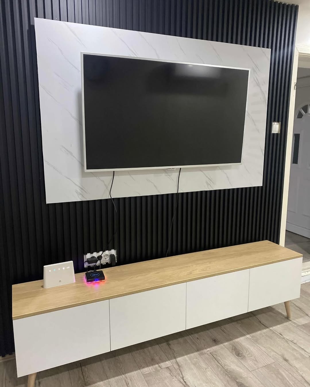 Wall-mounted flat screen TV above a wooden and white cabinet with black vertical paneling behind.