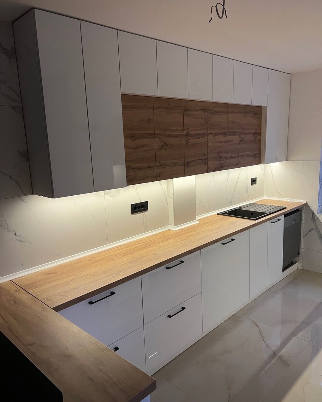 Wooden bed with beige upholstered headboard and footboard, white mattress, next to wooden nightstand with two drawers.